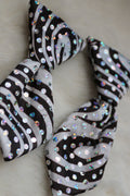 A black and white zebra-patterned neck tie embellished with iridescent sequins, displayed on a soft white faux fur surface.