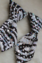 A black and white zebra-patterned neck tie embellished with iridescent sequins, displayed on a soft white faux fur surface.